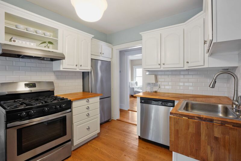 Kitchen with stainless appliances, butcher block counters and subway tile, looking in the hallway and onto a bedroom.
